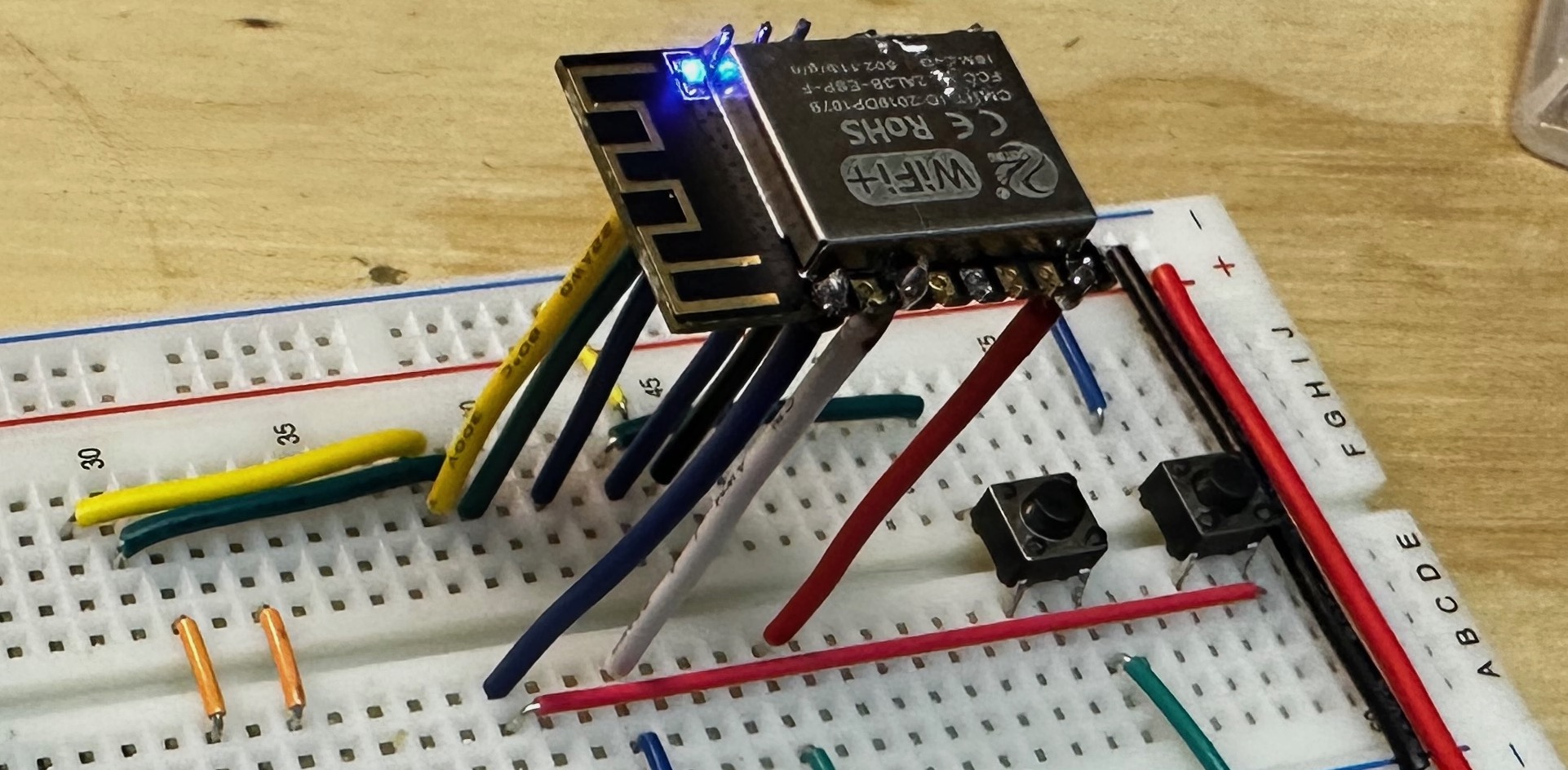 The ESP-12E suspended above a breadboard by some crudely soldered-on wires.